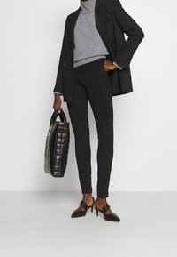 Zwarte slim-fit broek gecombineerd met een grijze coltrui en een op maat gemaakte zwarte blazer. Geaccrediteerd met een gequilt zwarte handtas.