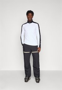 Valge, pika varrukaga, neljandiku tõmblukuga topp mustade aktsentidega; kombineeritud mustade pükstega, millel on kreemikad tõmblukud ja sirge lõige.