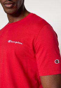 Κόκκινο βαμβακερό κοντομάνικο T-shirt με κεντημένο λογότυπο "Champion" στο στήθος και μικρότερο λογότυπο στο μανίκι.