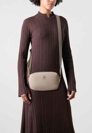 Mujer que lleva un vestido marrón acanalado de manga larga con un bolso bandolera beige que presenta un logo metálico en el frente.