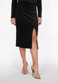 Zwarte midi rok met een zijsplit, van gestructureerde stof met een diamantpatroon, gecombineerd met gouden sandalen met banden.