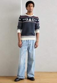 Tmavomodrý pletený sveter so vzormi sobov a snehových vločiek; krémové akcenty, dlhé rukávy, rebrované manžety, v kombinácii so svetlomodrými džínsami s širokými nohavicami.
