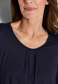 Dunkelblaues Oberteil mit runder Ausschnitt und Faltendetail an der Vorderseite. Weicher Stoff mit glatter Textur, enganliegendes Design im Schulterbereich.