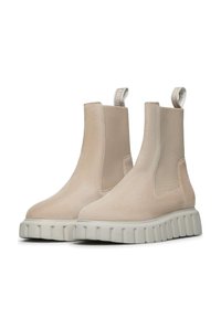 Beige semišové kotníkové boty s elastickými bočními panely, robustní bílá gumová podrážka a poutko na zadní straně pro snadné obutí.