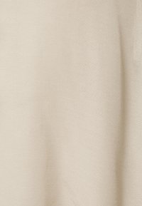 Tessuto beige che mostra una superficie liscia e texture con una leggera lucentezza. Il materiale sembra leggero e si drappeggia dolcemente, senza motivi visibili.