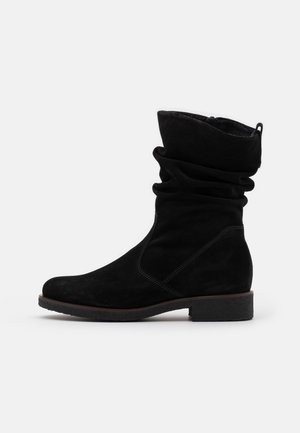 Botte en daim noir mi-mollet décontractée, avec petit talon et bout arrondi, dotée d'une languette à l'arrière et de détails cousus sur un fond uni.