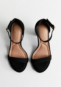 Sandali neri con tacco alto in morbido suede, con una fascia larga sulla parte anteriore e una sottile cinghia alla caviglia, dotati di una soletta beige.