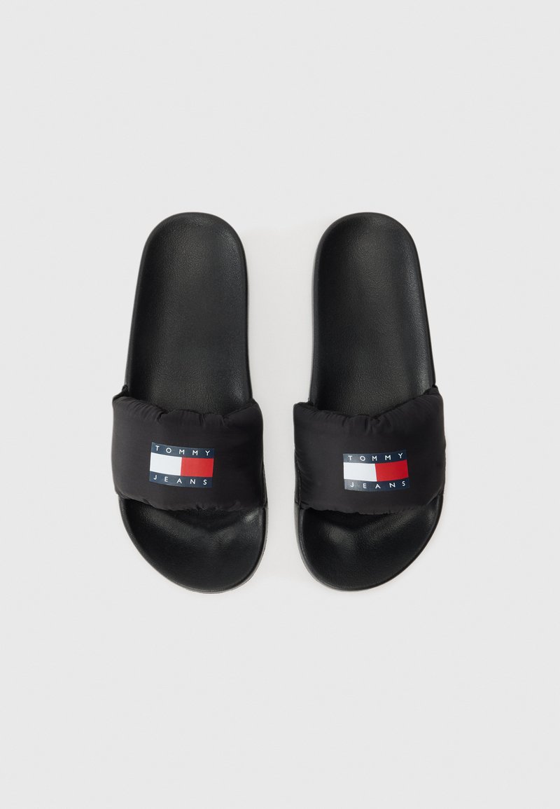 Schwarze Rutschsandalen mit einem gepolsterten schwarzen Riemen, der ein Farbkasten-Logo in Rot, Weiß und Blau zeigt. Glatte Sohle und einfache Form.