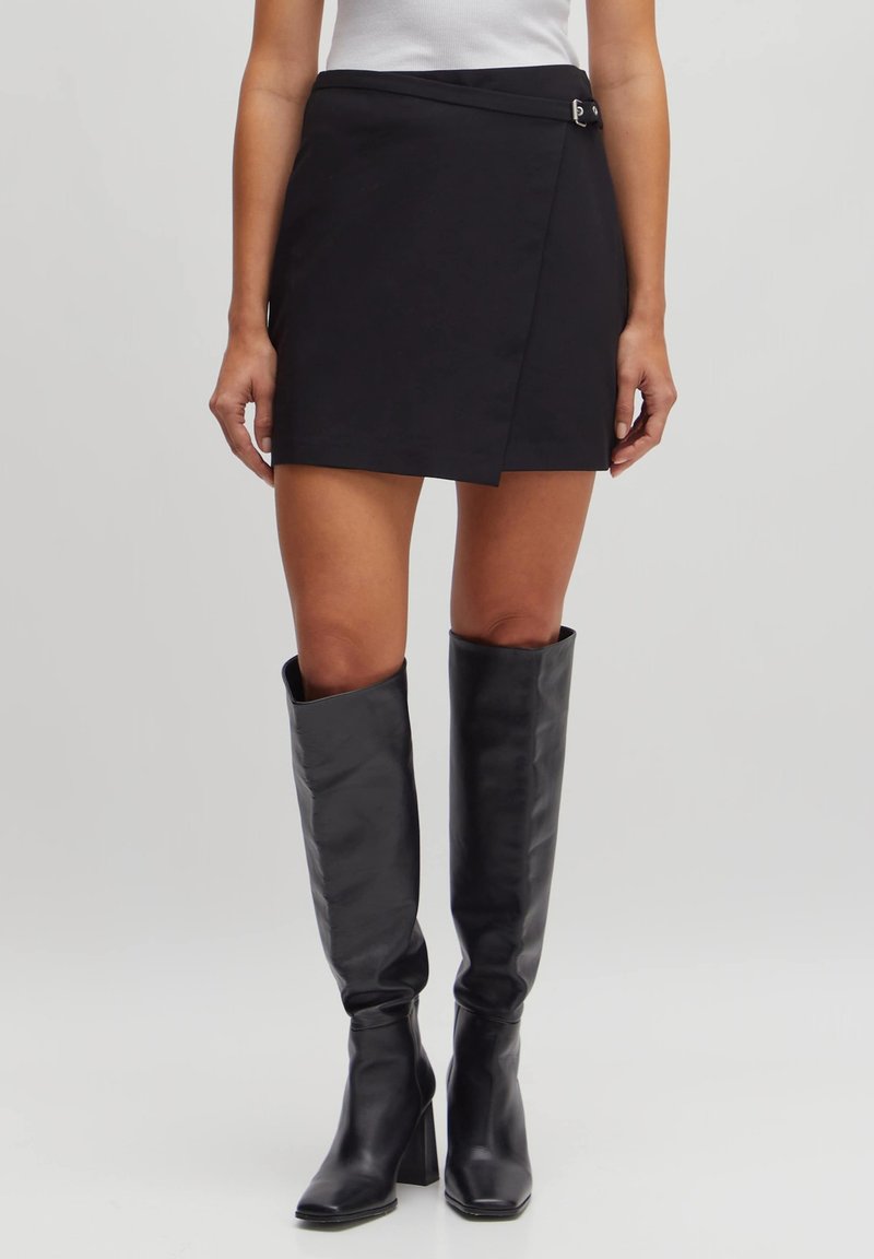 Zwarte wikkelrok gemaakt van gladde stof met een zijsluiting en een strakke silhouet, gecombineerd met zwarte leren laarzen tot de knie.