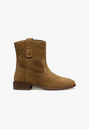 Botín de ante marrón con tacón bajo, tira de agarre y puntera redondeada, exhibido sobre un fondo blanco.