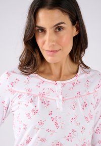 Pigiama con maniche lunghe in cotone bianco con motivo floreale rosa, dotato di scollatura rotonda, apertura con bottoni e profilo rosa chiaro.