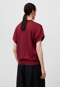 Top corto bordeaux con una vestibilità rilassata, bordo elastico e trama liscia. Abbinato a pantaloni scuri e larghi.