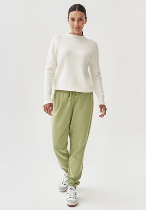 Pulover alb din tricot cu guler diamantat, asortat cu pantaloni de trening verzi prevăzuți cu un elastic la talie și adidași albi cu accente gri.