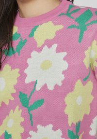 Pull en maille avec une base rose ornée de grands motifs de marguerites blanches et jaunes, de feuilles vertes, et un col rond côtelé.