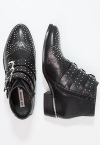 Botas ankle de cuero negro con adornos de tachuelas, con una correa con hebilla y un tacón bajo, diseñadas con un acabado texturizado.