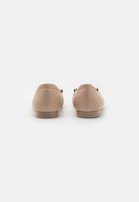 Mocasines de cuero beige con la parte trasera texturizada, pequeño tacón de madera y acentos en tono dorado en los laterales.