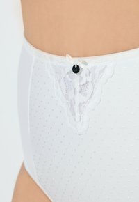 Bílé vysoké kalhotky s puntíkovanou texturou, krajkovým lemem v pase a drobnou mašlí s kulatým černým knoflíkem jako akcentem.