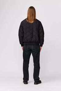Veste bombardier noire matelassée avec des poignets et un ourlet côtelés, associée à un jean en denim foncé et des chaussures noires. La vue arrière montre les textures et les détails de couture.