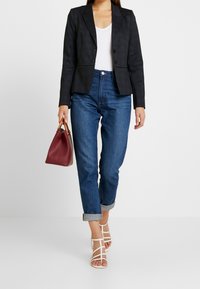 Dark gray structured blazer, white v-neck shirt, rolled blue jeans, white strappy sandals, and a maroon handbag.
