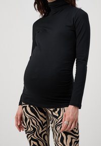 Svart långärmad topp med hög halsringning, med en figursydd design. Kombinerad med beige leggings som har ett djärvt svart zebramönster.