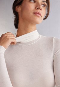 Vit långärmad åtsittande topp med hög krage och mjukt, halvgenomskinligt tyg, med en slät yta och minimala sömnadsdetaljer.