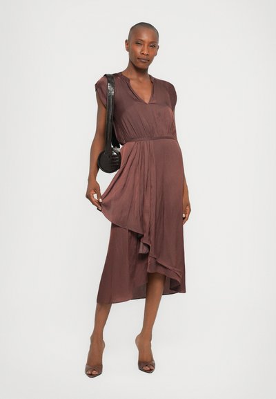 Robe midi bordeaux à manches courtes, décolleté en V, taille froncée et ourlet asymétrique. Associée à un sac bandoulière circulaire noir et des talons.