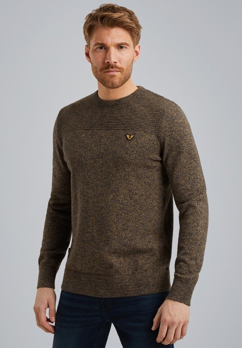 Pull en tricot brun avec une texture côtelée et un col rond. Présente un petit logo sur la poitrine, des poignets ajustés et un ourlet droit.