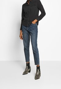 Black button-up shirt with two front pockets, paired with medium blue straight-leg jeans and black and silver snake-print ankle boots.