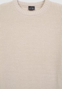 Beżowy sweter z dzianiny z okrągłym dekoltem, z teksturowanym wzorem i ściągaczami na rękawach, wykonany z miękkiego materiału. Metka widoczna przy dekolcie.