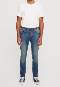 Mörkblå denimjeans för män med en avsmalnande passform, subtila blekningar, fem-fickorsdesign och knappstängning, i kombination med en enkel vit t-shirt.