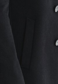 Czarny wełniany płaszcz o teksturowanym wykończeniu, z boczną kieszenią i jasnymi guzikami na przedniej listwie.