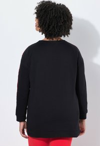 Zwarte sweatshirt met lange mouwen, voorzien van een rode accent langs de schouders. Glad textuur, ontspannen pasvorm en ronde halslijn.