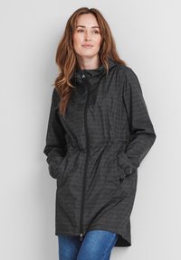 Black zip-up jacket with a textured pattern, features a hood, adjustable waist, and side pockets. Accompanied by blue jeans.