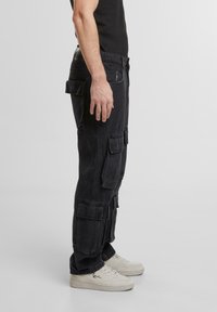 Pantaloni cargo negri din denim, cu multiple buzunare mari, o croială relaxată și o textură ușor uzată. Îmbunătățiți cu o închidere cu nasture.