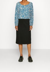 Top a maniche lunghe con stampa floreale blu e scollatura ampia, abbinato a una gonna nera fino al ginocchio e mocassini neri. Tessuto dalla texture liscia.