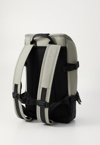 Grauer Rucksack mit glatter Außenseite, Netzrücken, gepolsterten Schulterriemen und schwarzen Akzenten. Verfügt über verstellbare Riemen und einen oberen Griff.