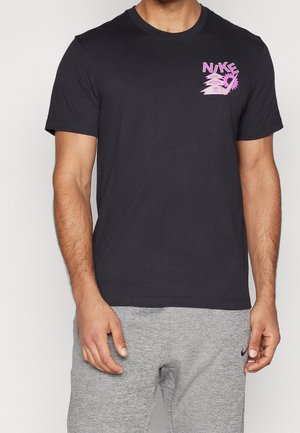Homme portant un t-shirt noir Nike avec un graphisme rose sur la poitrine et un pantalon de survêtement gris avec un petit logo Nike noir.