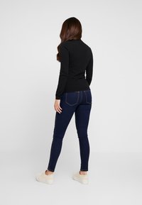 Camiseta negra de manga larga con diseño ajustado, combinada con jeans skinny azul oscuro con un ligero brillo y costuras contrastantes. Zapatillas de plataforma crema.