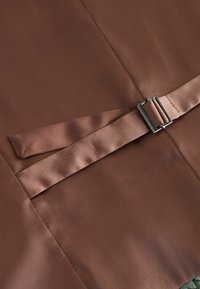 Barna selyemszatén anyag széles pánttal és fém csattal, sima, elegáns felületet képezve. A hátlap egy finoman texturált anyag.