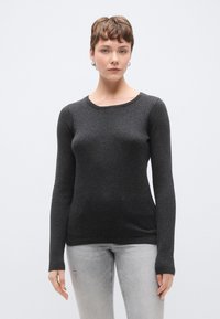 Μαύρο πουλόβερ με μακριά μανίκια, υφασμάτινη υφή, στρογγυλή λαιμόκοψη και εφαρμοστή γραμμή. Συνδυάζεται με ανοιχτό γκρι τζιν με φθορές.