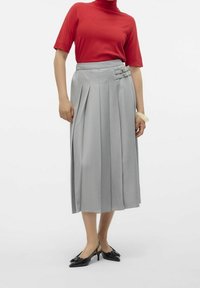 Gonna midi plissettata grigia con due dettagli a fibbia, abbinata a un dolcevita rosso a maniche corte. Scarpe nere con punta appuntita completano il look.