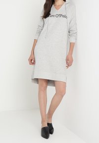 Grau Hoodie-Kleid mit V-Ausschnitt, langen Ärmeln und Kordelzug. Mit schwarzem Text "Marc O'Polo" auf der Brust und seitlichen Schlitzen am Saum.