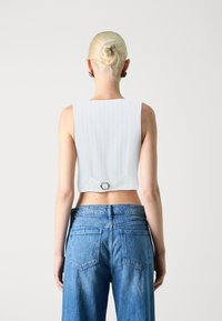 White ribbed crop top with a square back and small buckle detail, paired with high-waisted blue denim jeans featuring two back pockets.