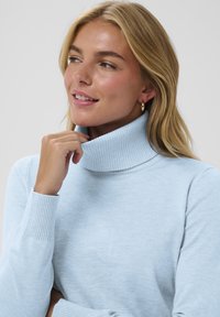 Ljusblå polotröja gjord av mjukt, ribbat stickat material. Har en hög krage och figurnära långa ärmar.