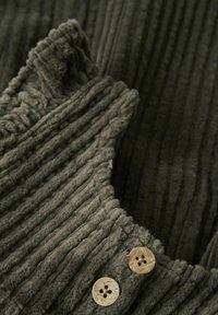 Tissu côtelé vert olive avec une texture douce, présentant un bord festonné et deux boutons en bois avec des découpes en forme de fleur.