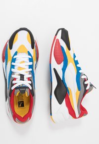 Chaussures de sport avec une tige en mesh ornée d'accents multicolores en jaune, bleu, rouge et noir. Semelle texturée et lacets blancs.