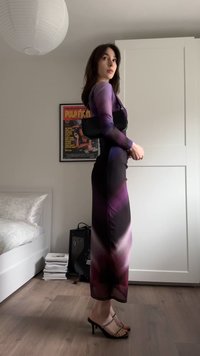 Paarse en zwarte kleurovergang jurk met lange mouwen, nauwsluitend design. Zwarte handtas en sandalen met hoge hak en bandjes maken de look compleet.