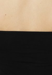 Zwarte ribstof band rond de taille, met daarboven glad beige huid. Schone randen zonder zichtbare hardware of patronen.