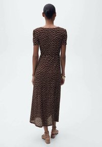 Rochie midi cu buline maro, cu mâneci puff scurte, talie ajustată și fustă vaporos; purtată cu sandale platformă maro, textură netedă.