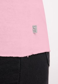 Roze stoffen T-shirt met een textuur gebreid, voorzien van een ruwe zoom en een klein grijs label met een hondenontwerp, gecombineerd met zwarte denim.